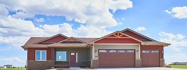 Red and gray Triple Dot ranch home beneath bright summer clouds